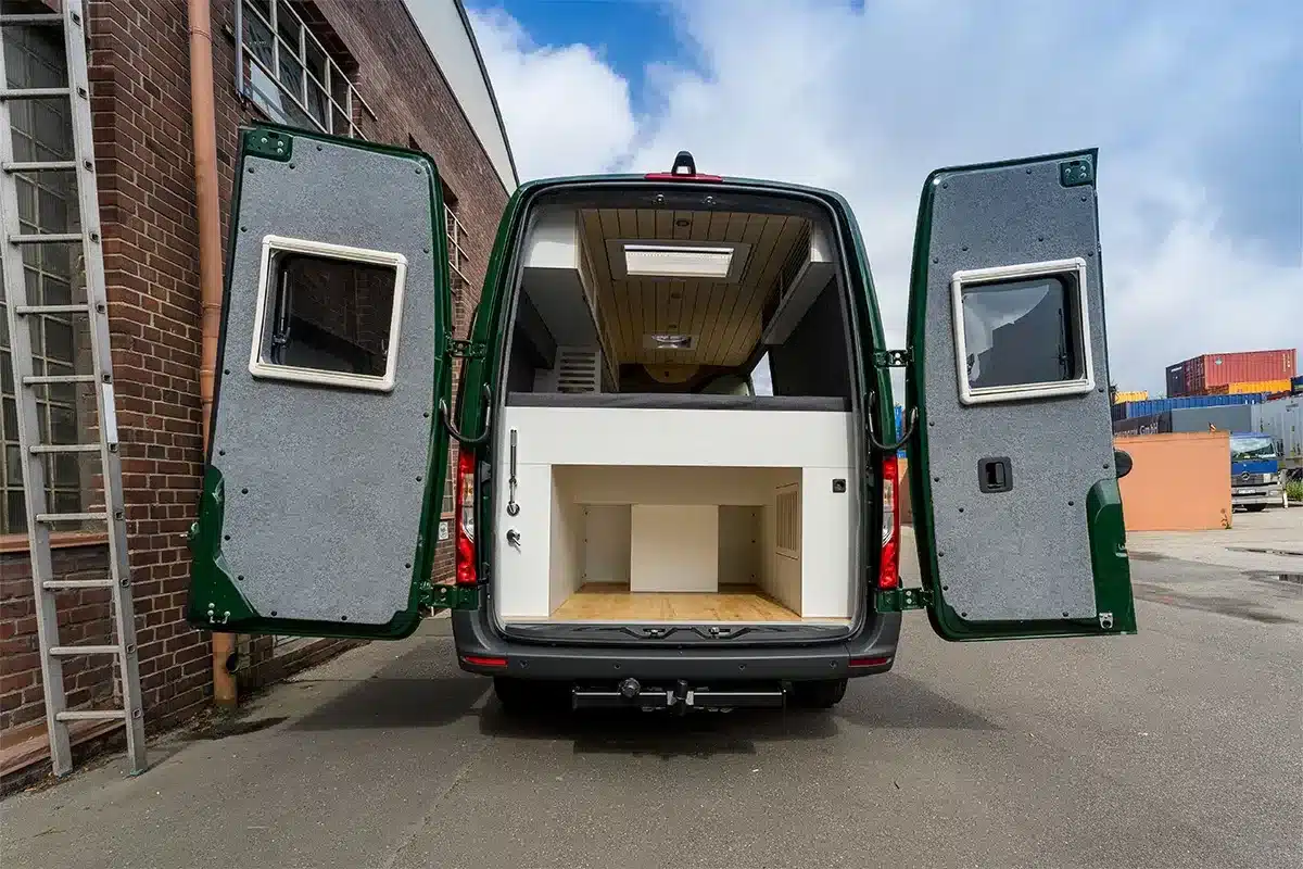 Blick durch die geöffneten Hecktüren des Libelle Campervans, gut sichtbar sind der Stauraum und Details des Innenausbaus.