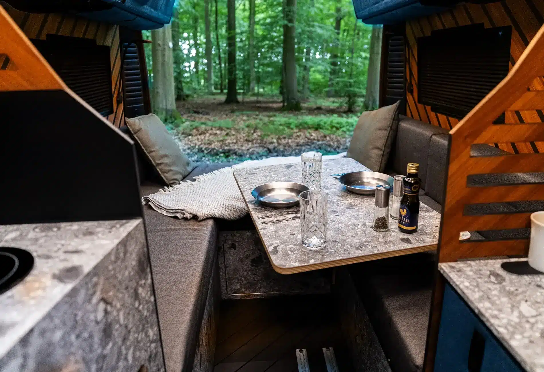 Innenraum des Light Arrow Kastenwagens mit Sitzlounge, Tisch und Ausblick in den Wald