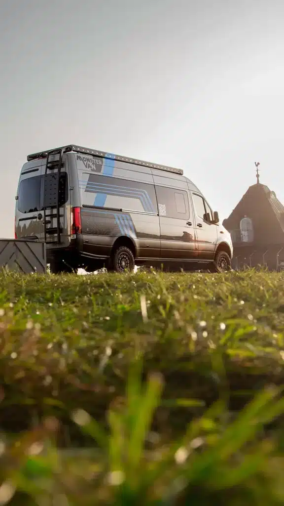 Heck- und Seitenansicht eines Major Monster 4x4 Campervans mit Leiter und Dachträger auf einem Mercedes-Benz Sprinter, abgestellt auf einer Wiese