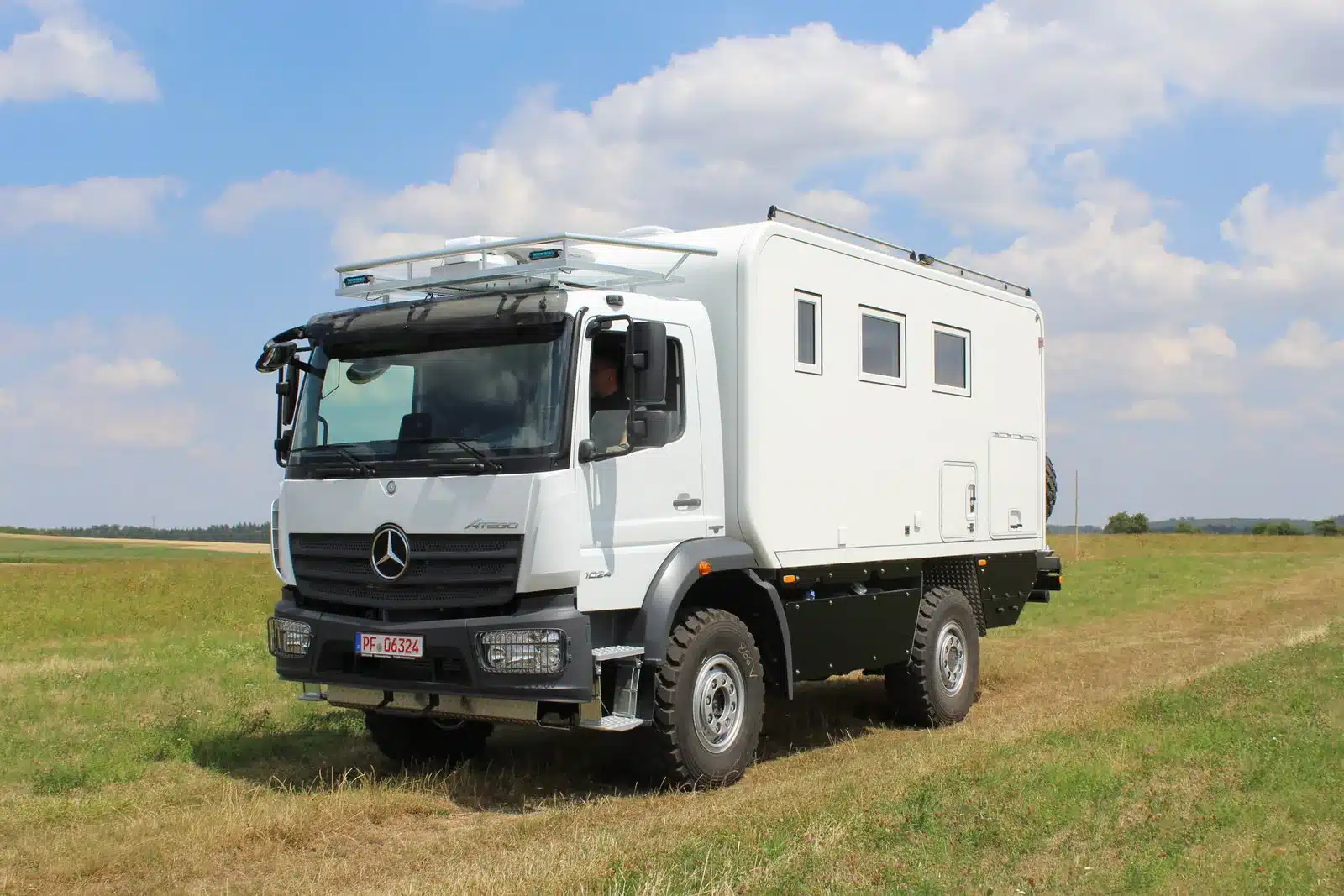 Seitenansicht eines weißen Mercedes-Benz Atego 1023 A 4x4 Expeditionsmobils auf einer Wiese unter blauem Himmel.