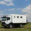 Expeditionsmobil Mercedes Benz Atego 1023 A 4x4 steht auf einer grünen Wiese unter leicht bewölktem Himmel.