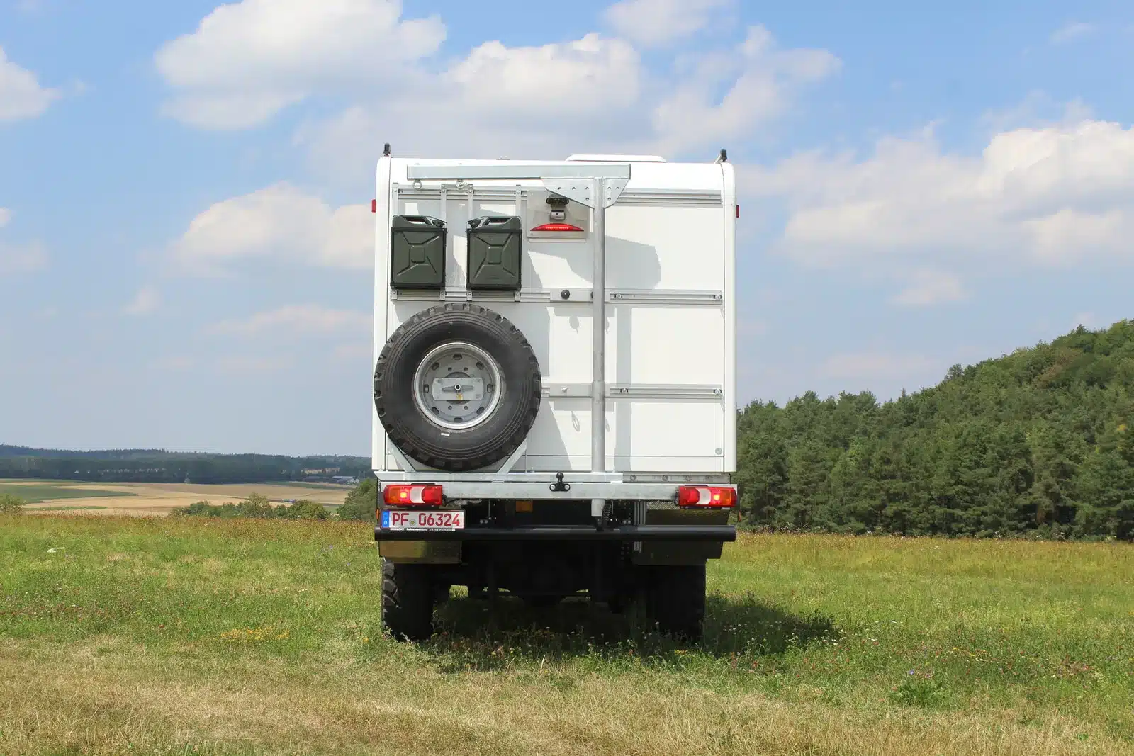 Mercedes-Benz Atego Expeditionsmobil von hinten mit Ersatzrad und Kanistern auf einer Wiese vor Wald und Feldern