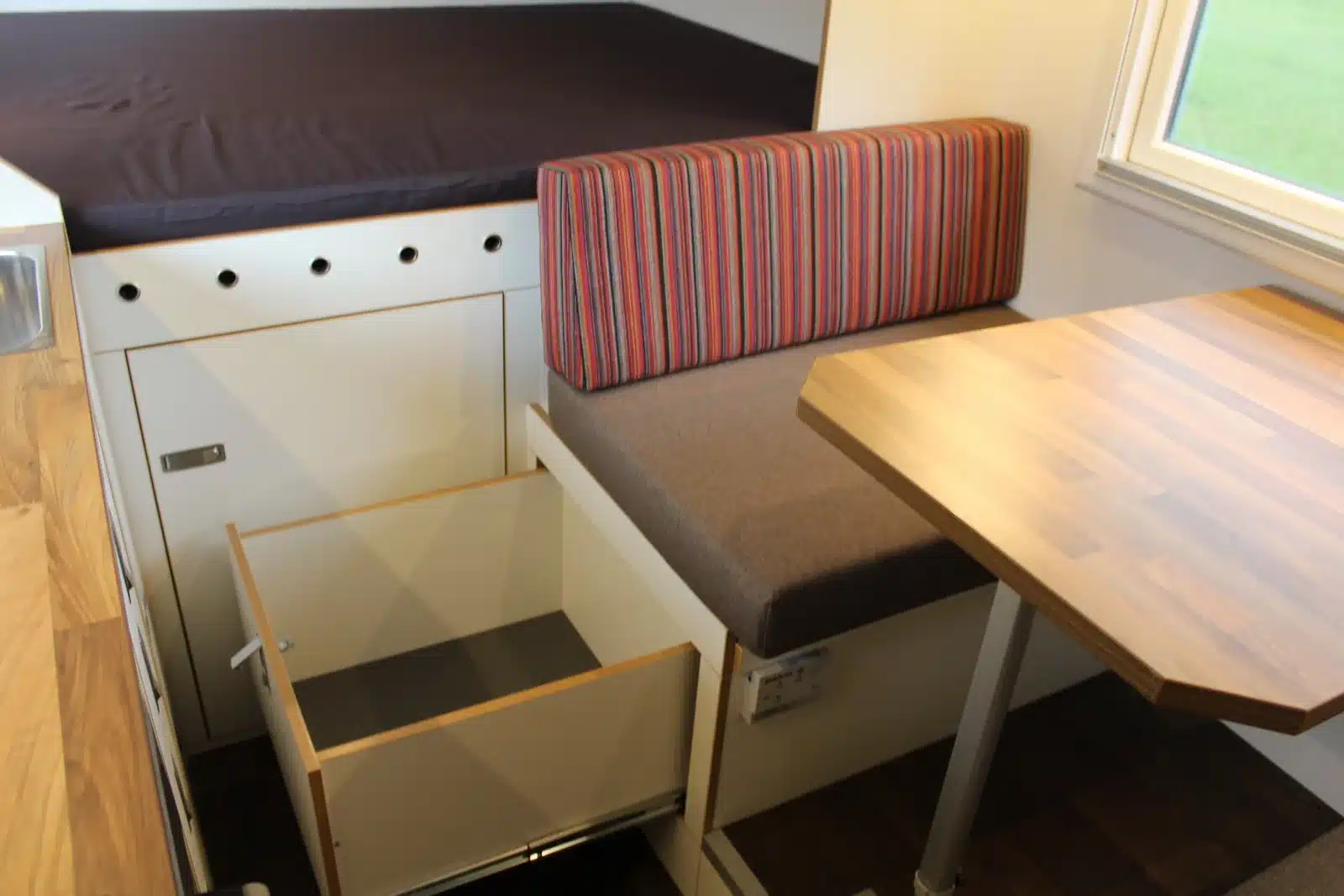 Innenraum des MB Atego 1225 AF 4x4 mit Sitzbank, Holztisch und Bett im Expeditionsmobil