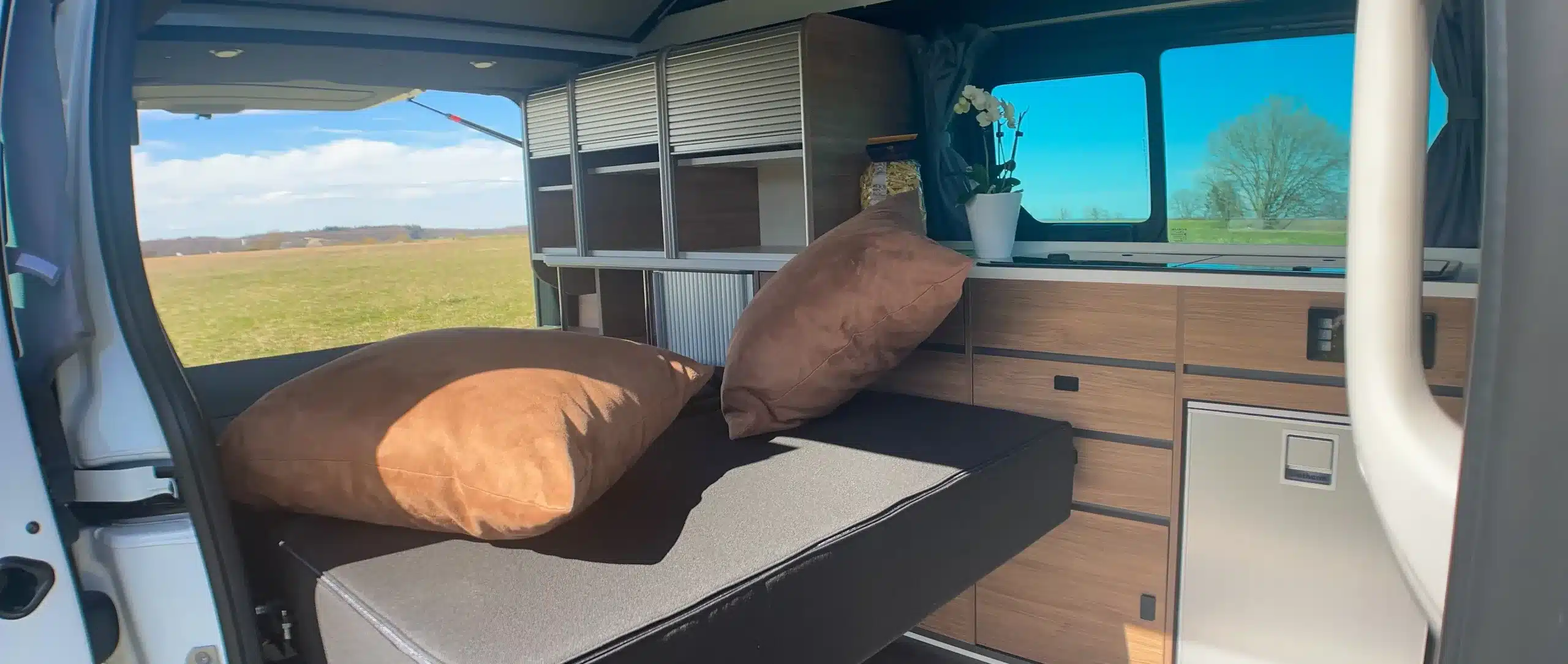 Innenraum eines Mooveo Campervan 3XL mit Bett, Sitzbank und Holzmöbeln