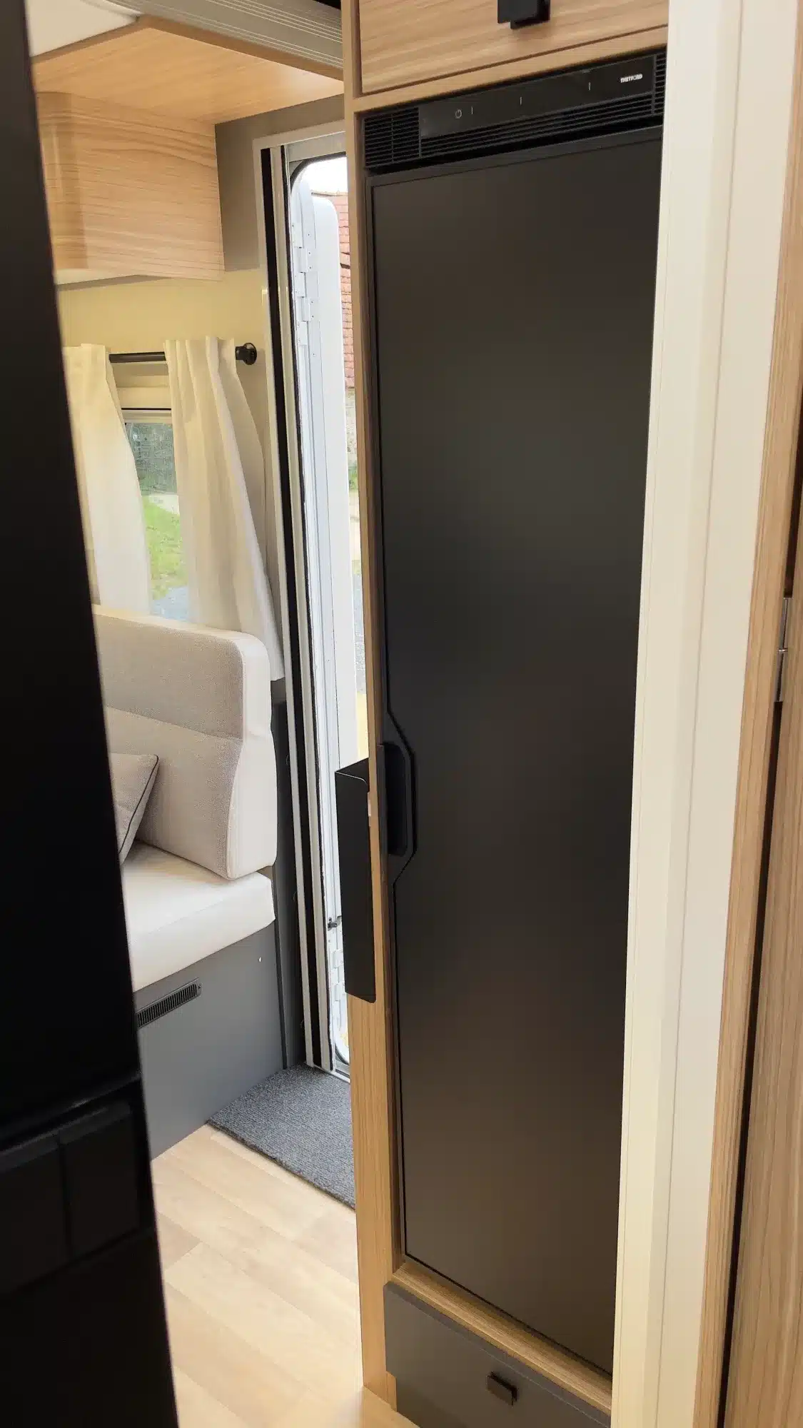 Kompressionskühlschrank im Innenraum eines MOOVEO TEI 74QB(F) Wohnmobils neben der Sitzgruppe und Eingangstür.