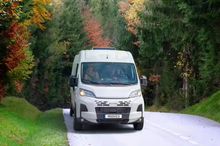 Weißer MOOVEO VAN 54DB Campervan fährt auf einer schmalen, von Bäumen gesäumten Straße