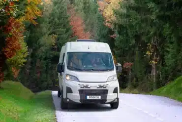 Weißer MOOVEO Kastenwagen auf einer kurvigen Straße im Wald