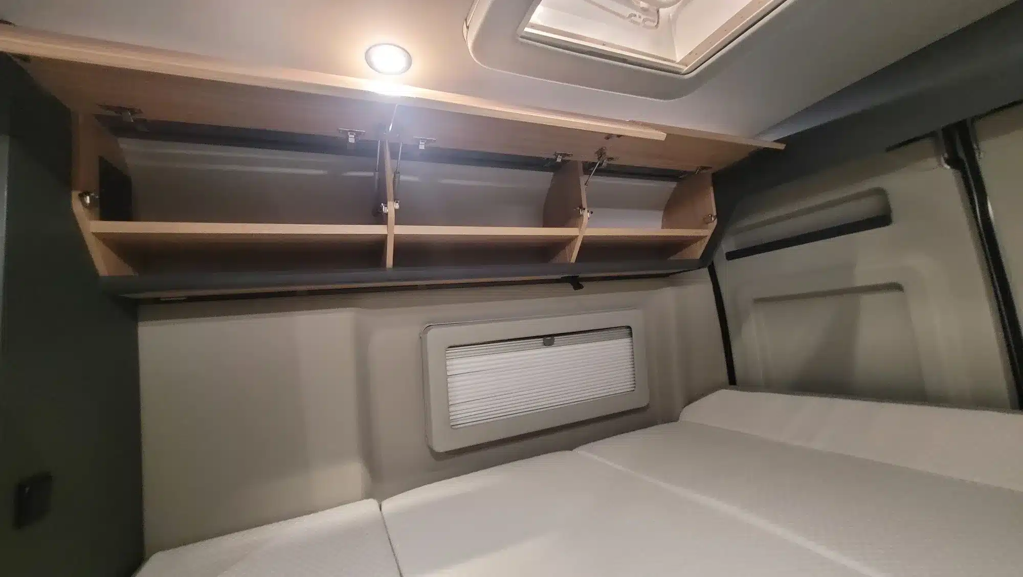 Schlafbereich im MOOVEO VAN 63EB mit Matratzen, Oberschränken, Seitenfenster und Dachfenster