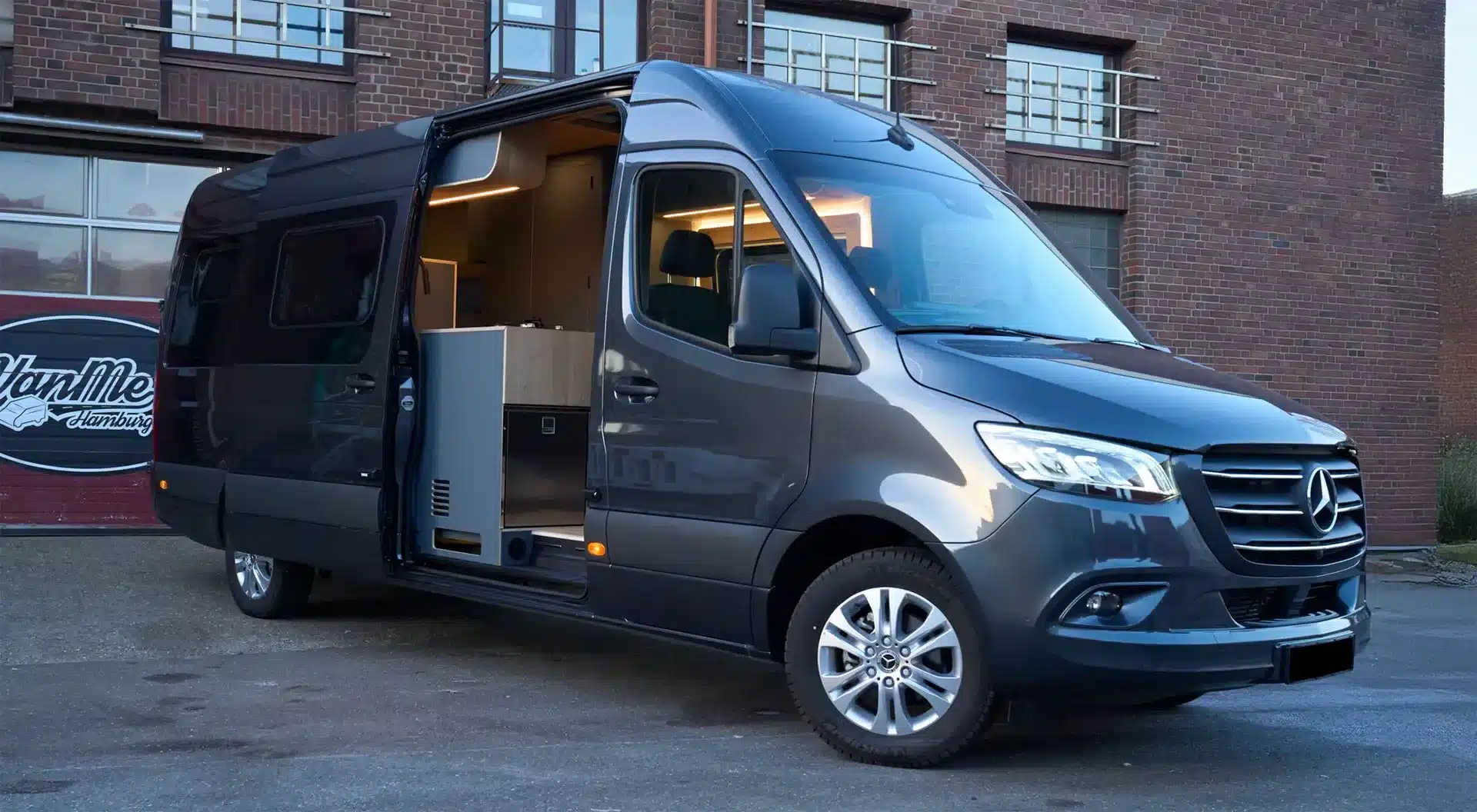 Morinter Campervan mit geöffneter Schiebetür, basierend auf einem Mercedes-Benz Sprinter, davor ein VanMe Hamburg Schild