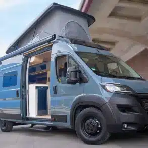 FIAT Ducato Multi Racer Campervan mit geöffnetem Aufstelldach auf einem Parkplatz, Schiebetür und Innenraum sichtbar.