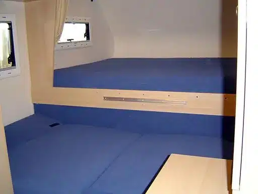 Blick auf das Alkovenbett mit blauen Polstern und Fenster in der GFK-Wohnkabine eines Nissan Navara Pickups