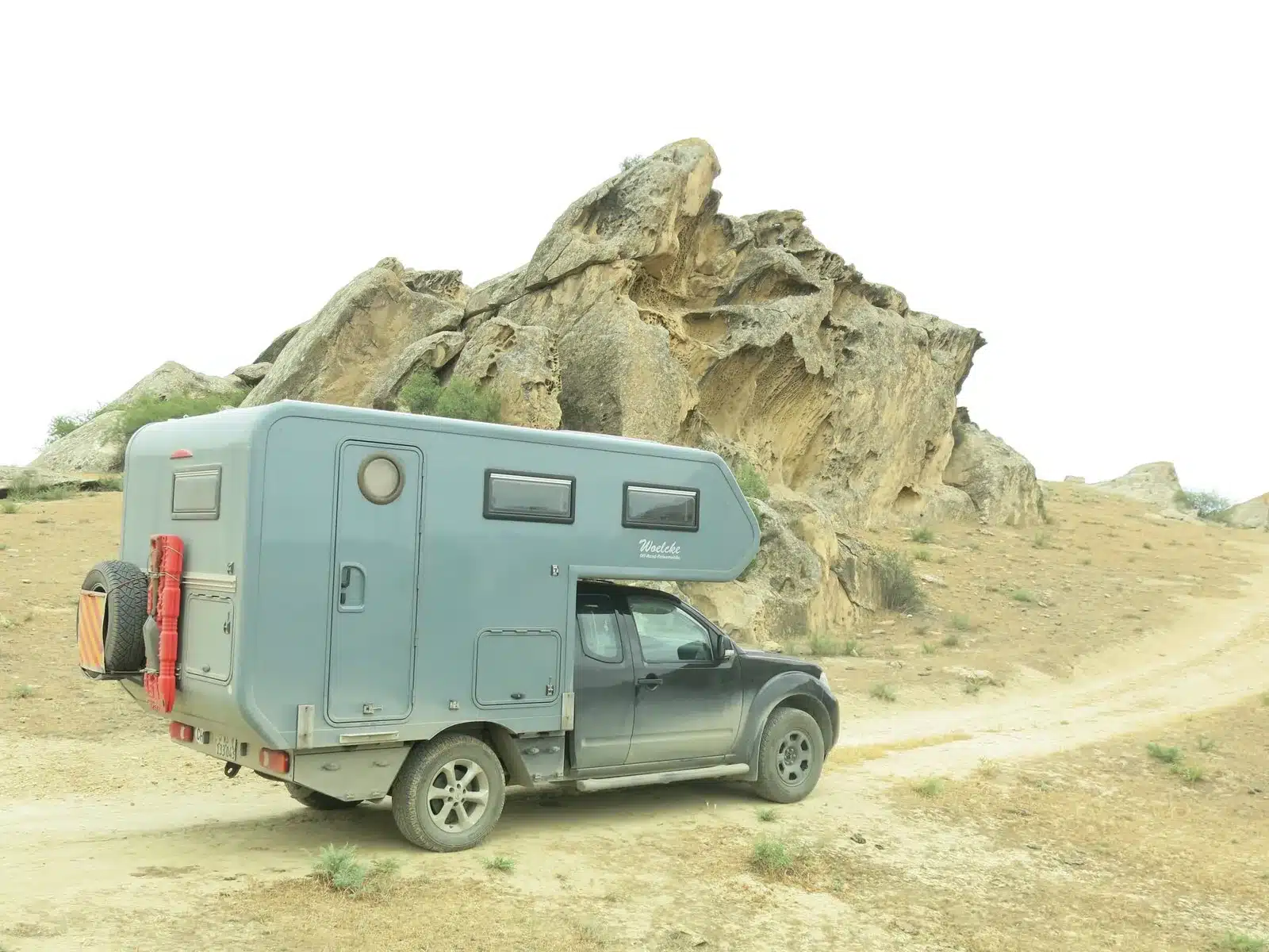 Absetzkabine auf Nissan Navara auf einer Schotterpiste vor Felsen, Offroad-Reisemobil