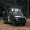 Noah Arche Campervan mit geöffneten Türen und eingeschalteter Beleuchtung, geparkt im Wald