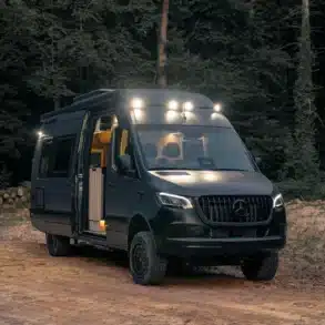 Noah Arche Campervan mit geöffneten Türen und eingeschalteter Beleuchtung, geparkt im Wald
