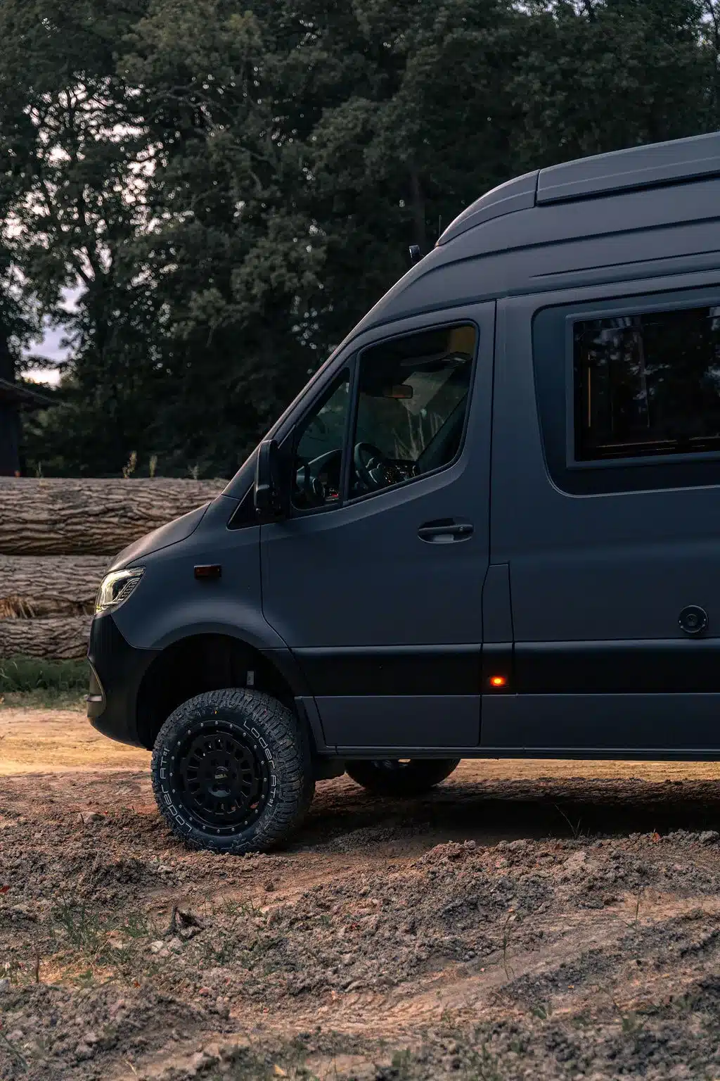 Seitliche Nahaufnahme des Noah Arche Campervans auf Mercedes-Benz Sprinter L3H3 Basis mit Offroad-Bereifung im Wald
