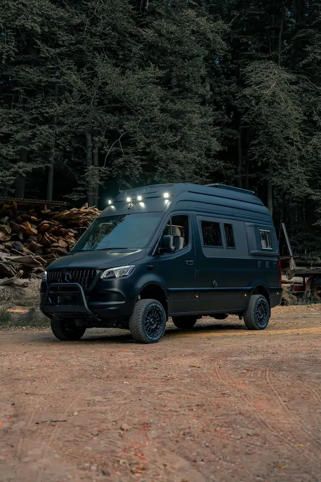 Noah Pulse Campervan auf Mercedes-Benz Sprinter-Basis mit Offroad-Elementen, stehend im Wald vor Holzstapeln