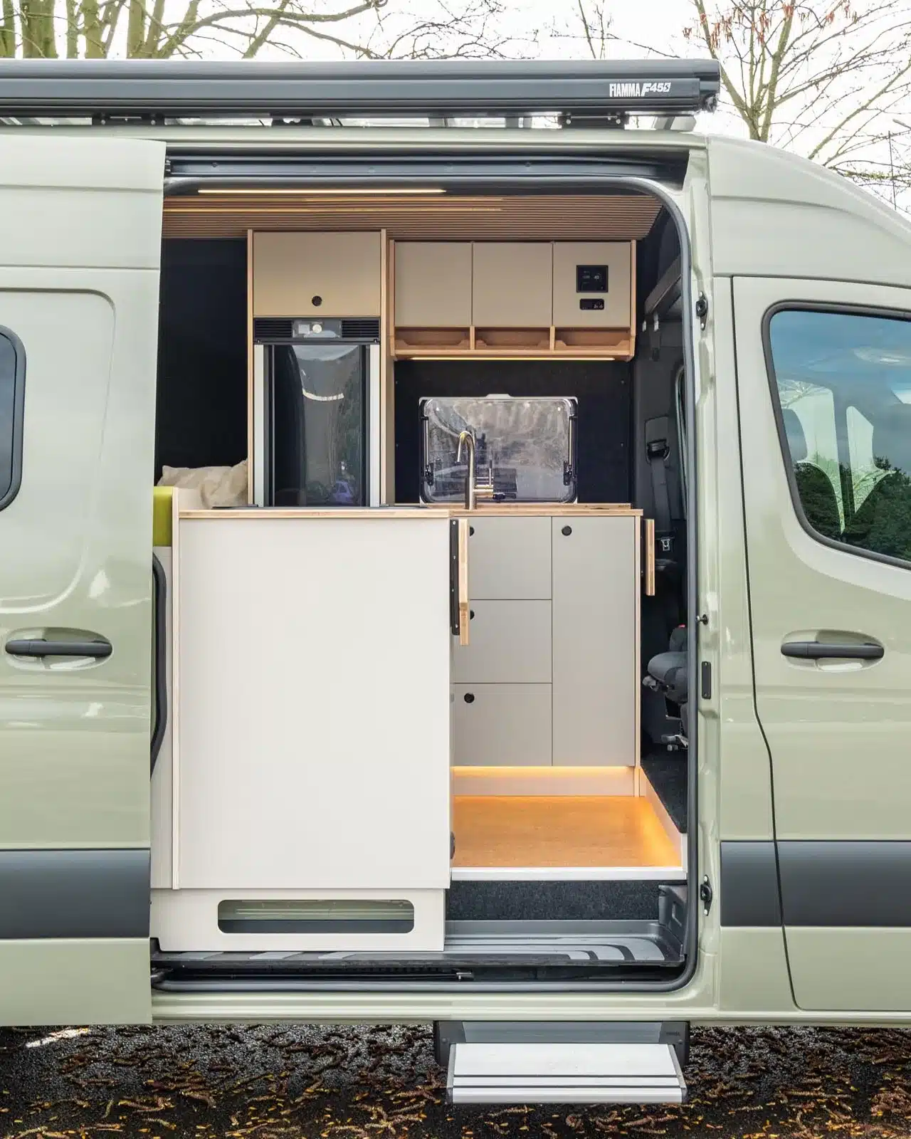 Offene Schiebetür eines ausgebauten Kastenwagens mit moderner Küchenzeile, Schränken und Stauraum