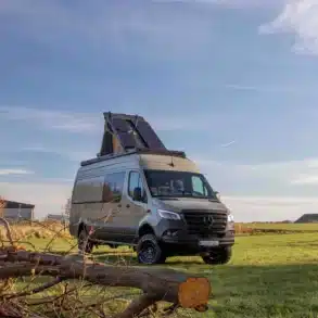 Mercedes Sprinter Campervan Sky Monster mit ausgeklapptem Dachzelt und Solarpanels, steht autark auf einer Wiese unter freiem Himmel.