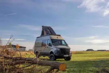 Mercedes Sprinter Campervan Sky Monster mit ausgeklapptem Dachzelt und Solarpanels, steht autark auf einer Wiese unter freiem Himmel.