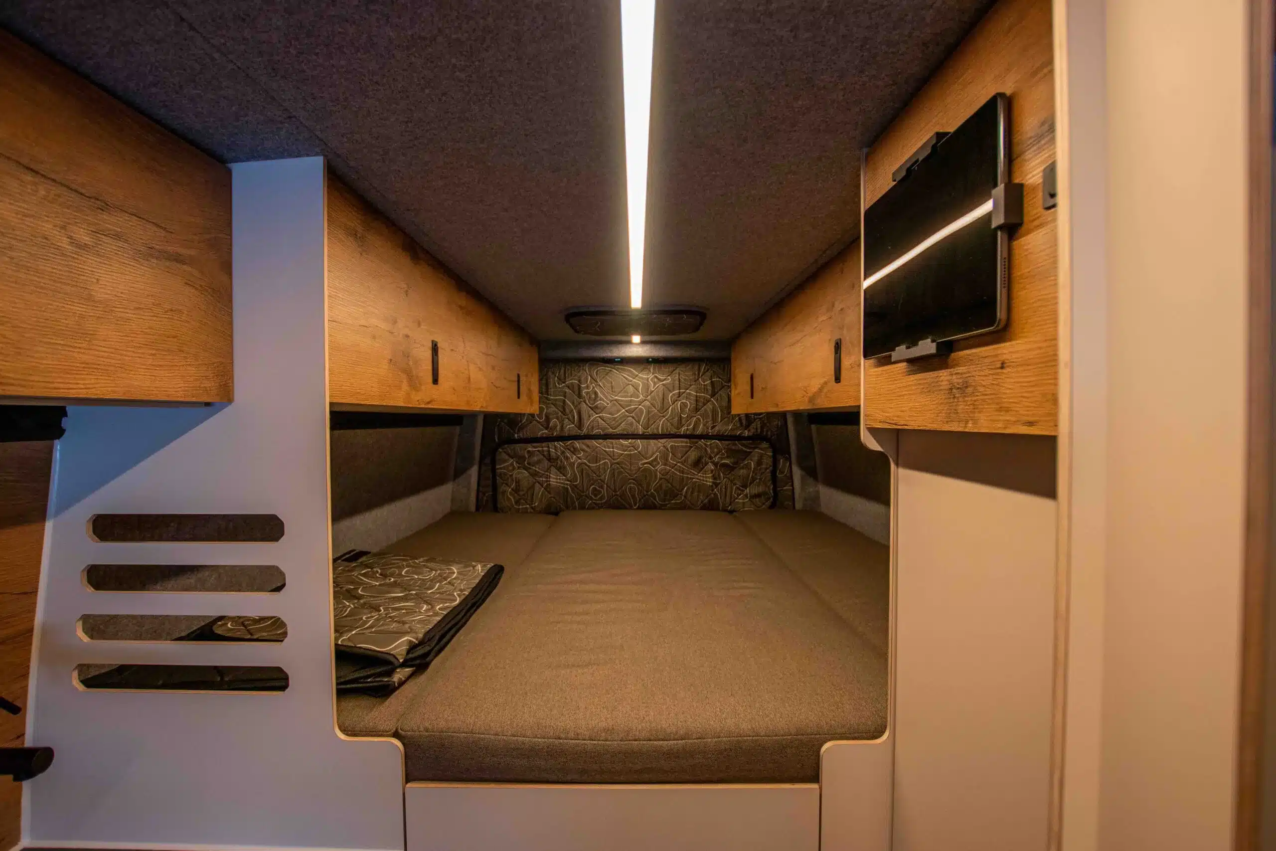 Innenansicht des Schlafbereichs im Mercedes Sprinter Sky Monster Camper mit Polstermatratze und Holz-Staufächern.