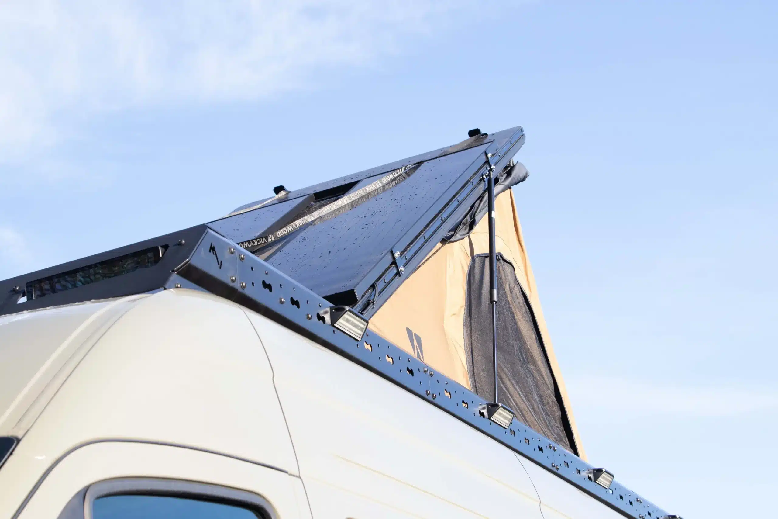 Geöffnetes Aluminium-Dachzelt mit Dachträger auf einem weißen Mercedes Sprinter Camper, Ansicht von der Seite vor blauem Himmel.
