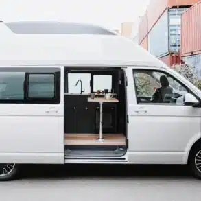 Seitenansicht des Streamline XL Campervans auf VW T6.1 Basis mit geöffnetem Hochdach und Einblick in den Innenraum mit Küchenzeile und Tisch.