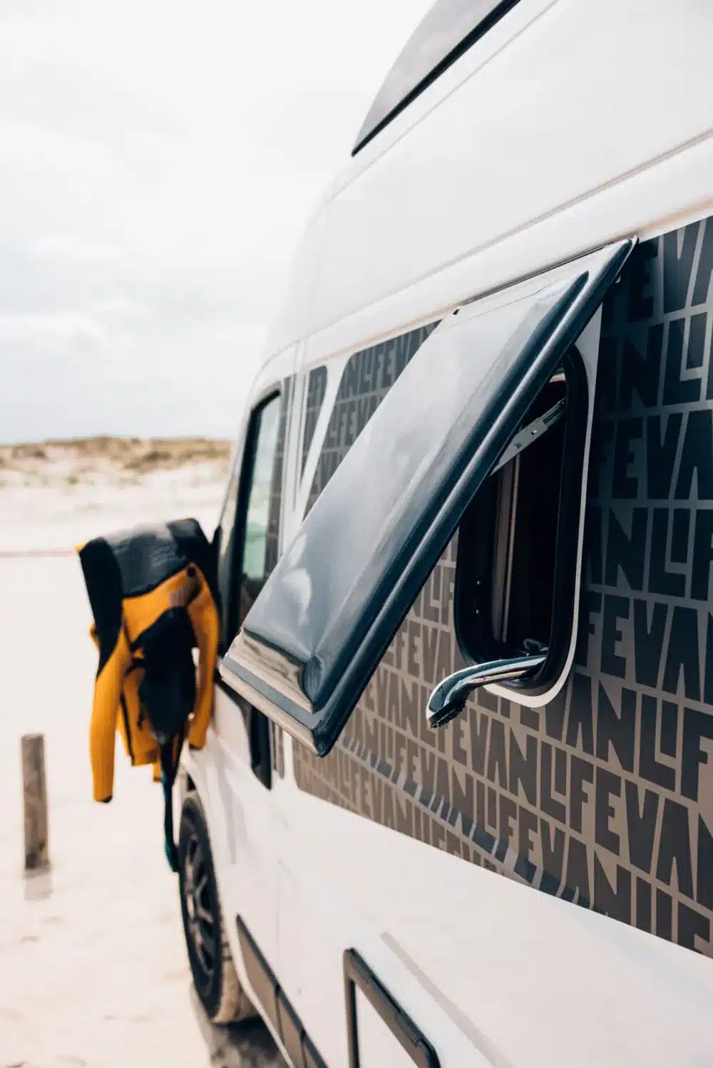 Geöffnetes Fenster eines Sunlight VANLIFE Campervans mit Neoprenanzug am Strand.