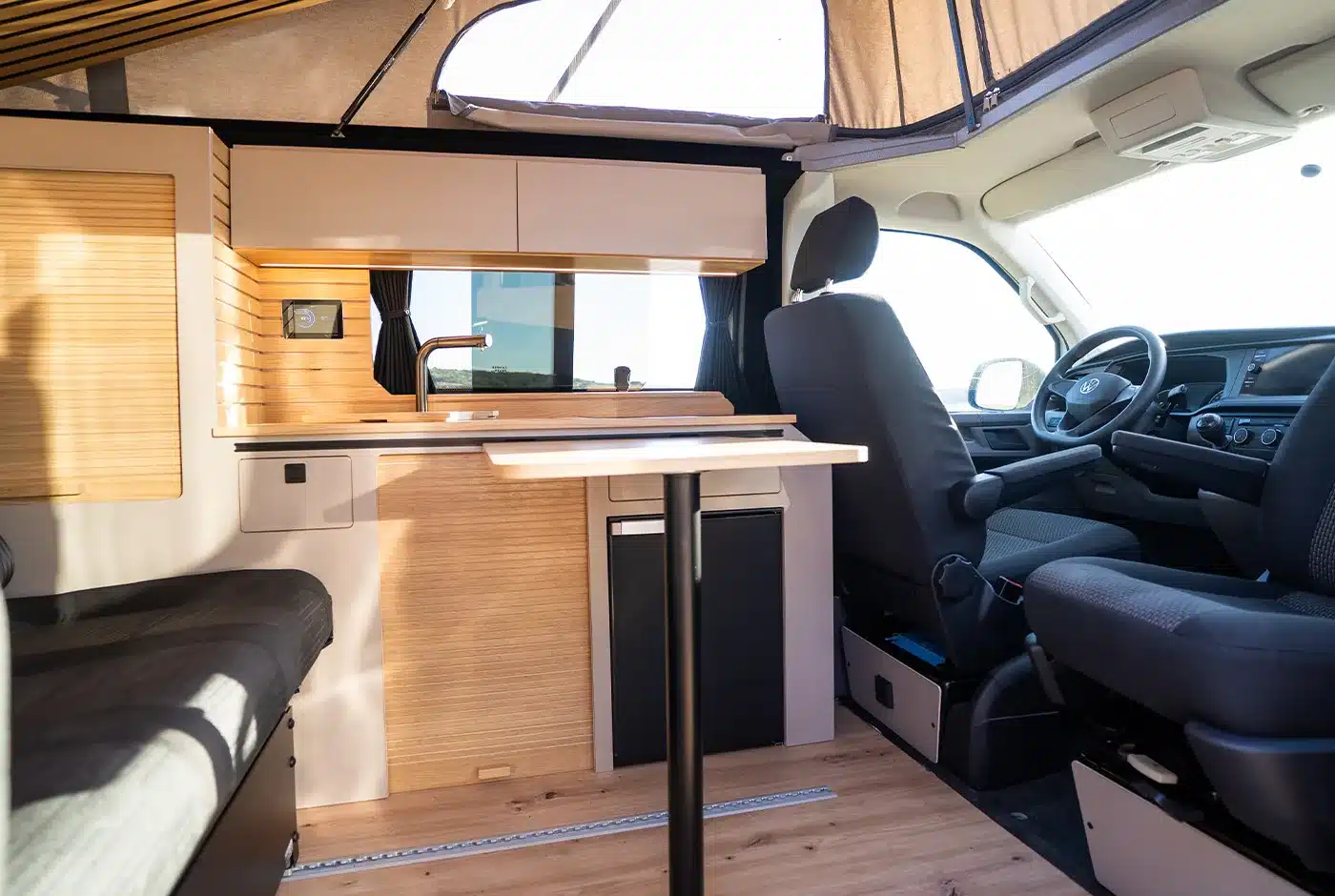 Innenansicht des VW T6.1 Expedition Pro mit Küche, Tisch und Fahrersitz
