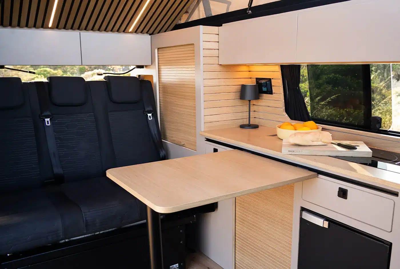 Moderne Campervan-Innenausstattung im VW T6.1 Expedition Pro mit Sitzbank, Tisch und Küche.