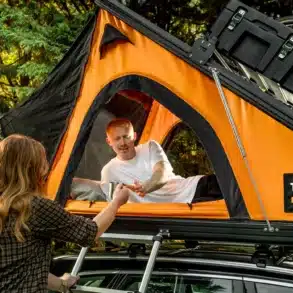Seitenansicht des geöffneten, orangefarbenen TentBox Cargo 2.0 Dachzelts auf einem Auto mit zwei Personen bei der Nutzung.