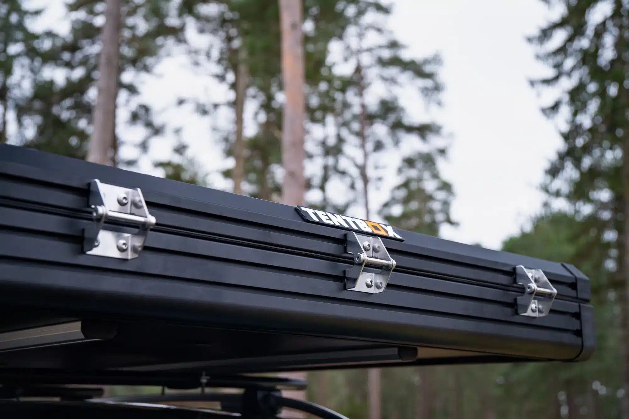 Nahaufnahme des geschlossenen TentBox Cargo 2.0 Dachzelts mit Aluminiumprofilen und Logo im Waldumfeld.