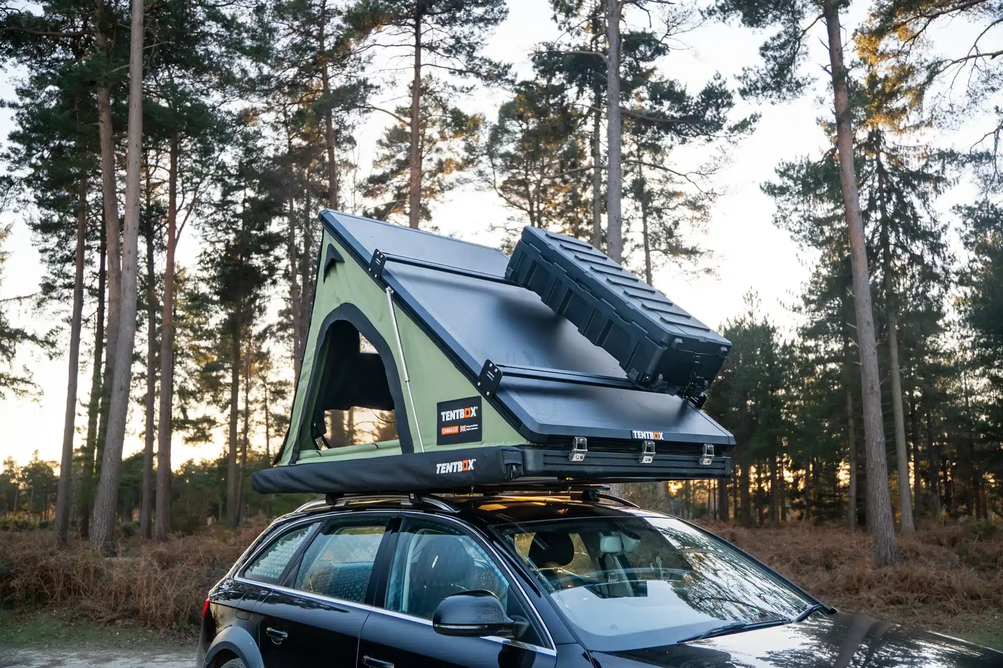 TentBox Cargo 2.0 Dachzelt montiert auf einem Auto mit zusätzlicher Transportbox auf dem Zelt, aufgenommen im Wald.