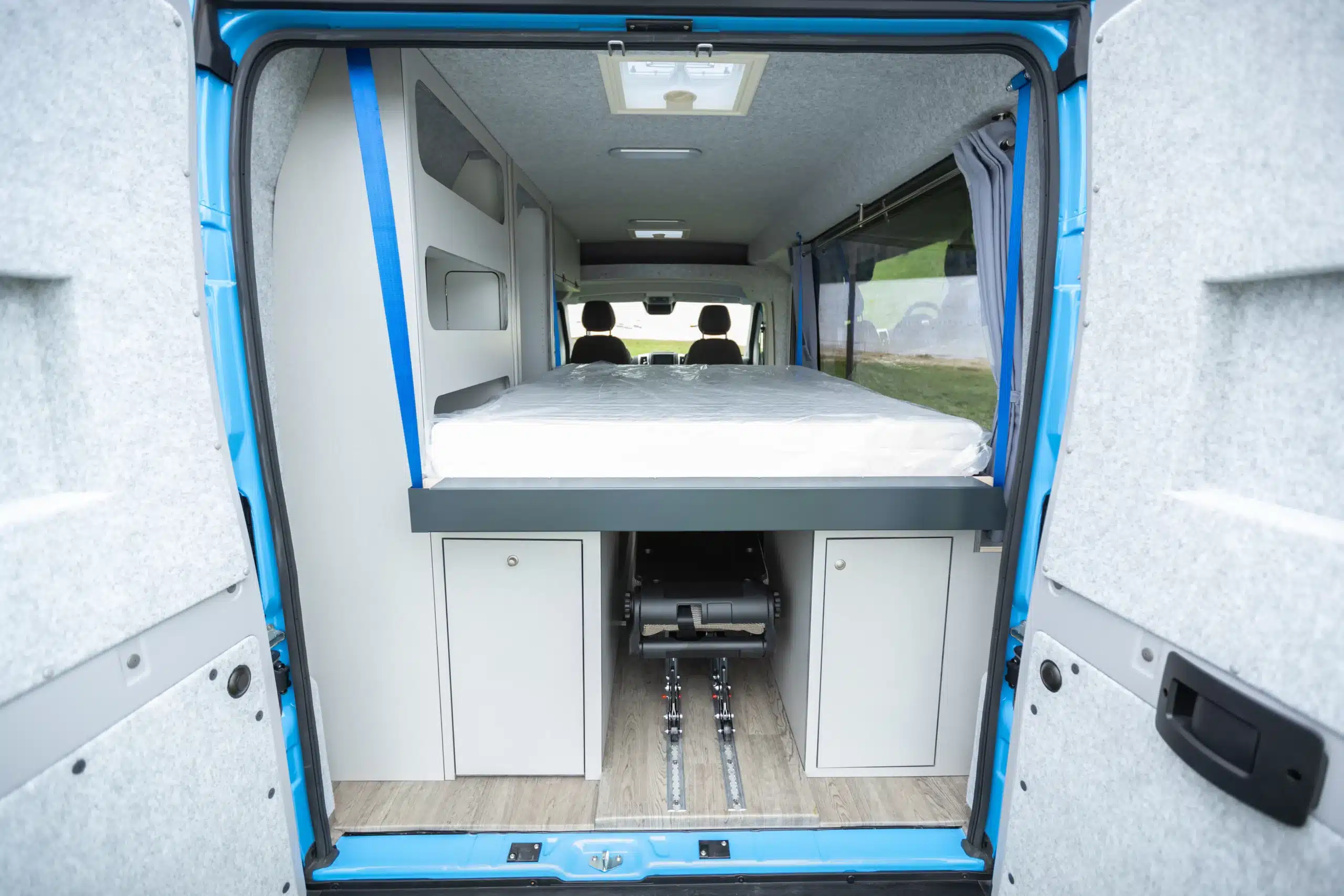 Innenraum des TIPI-Campingbusses mit abgesenktem Boden, Hubbett und Stauraum, gesehen von hinten.