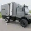 Unimog 435 Expeditionsmobil mit grauem Wohnaufbau, Leiter und Offroad-Bereifung