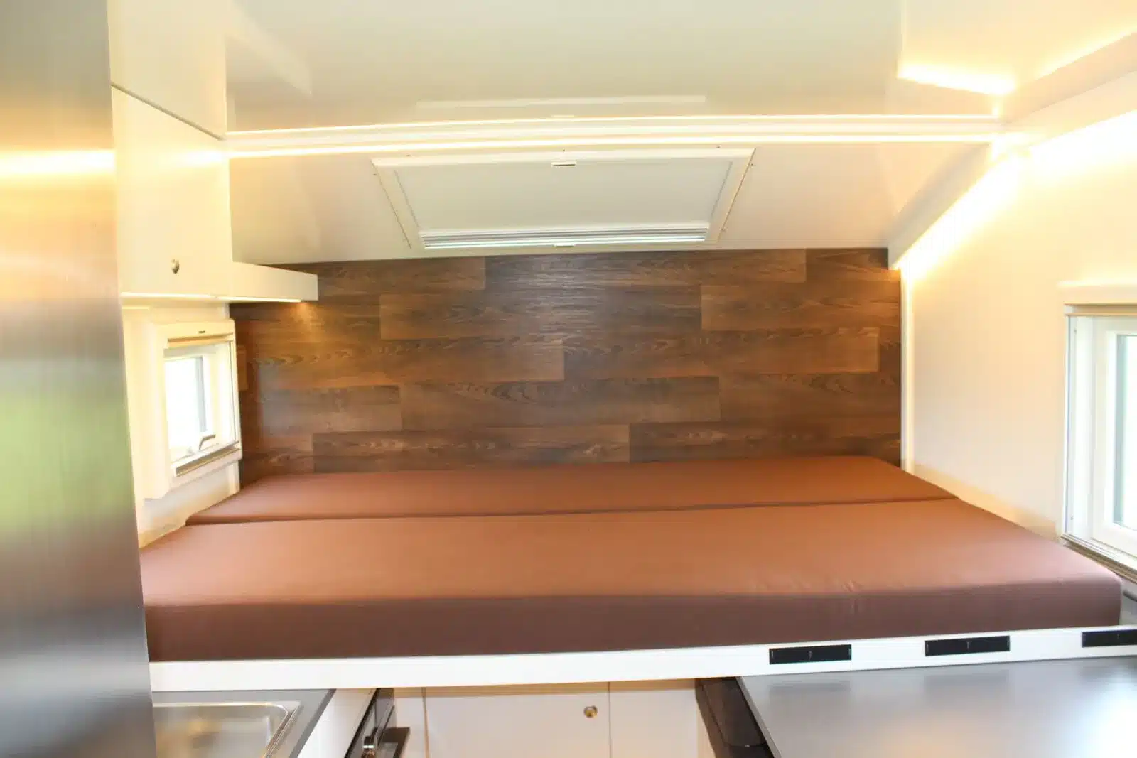 Blick ins Innere eines Expeditionsmobils mit Auszugsbett, Holzverkleidung und Fenster.