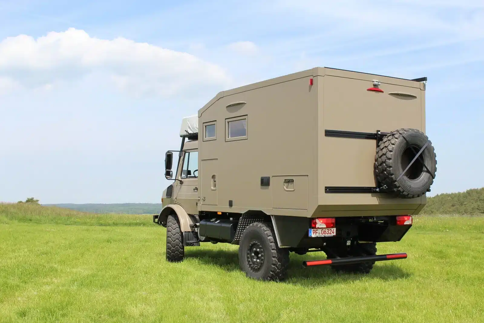 Unimog U1550L Expeditionsmobil mit Woelcke Wohnaufbau und Ersatzrad, fotografiert auf einer grünen Wiese bei Tageslicht