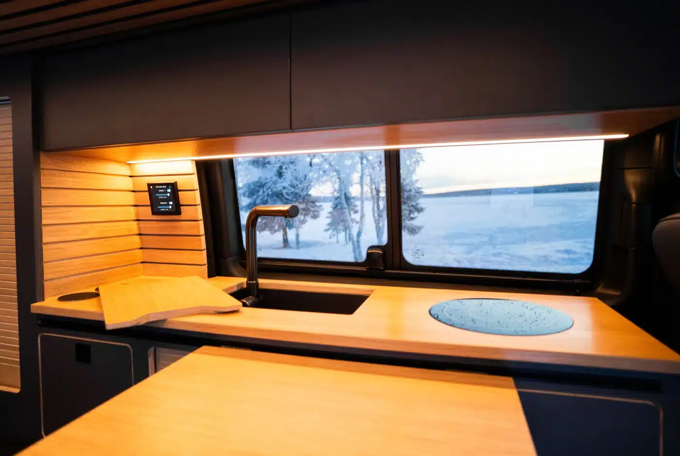 Küchenbereich im Mercedes V-Klasse Expedition Campervan mit Holzdekor und Fenster, dahinter verschneite Landschaft