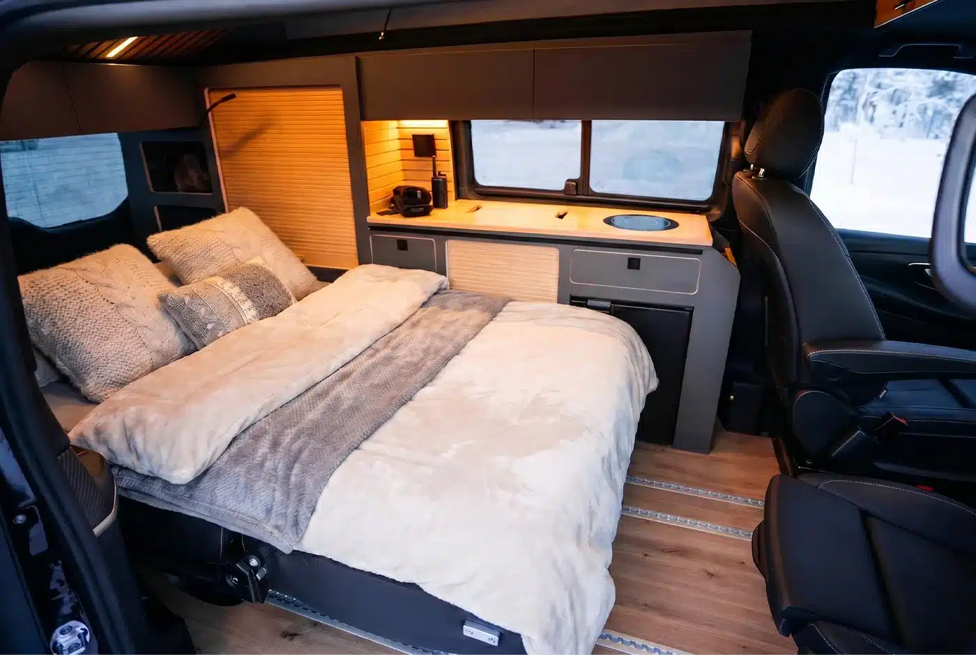 Wohnbereich der Mercedes V-Klasse Expedition mit ausgezogenem Bett, Kissen und integrierter Küchenzeile.
