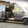Van in Black auf Mercedes-Benz Sprinter Basis mit geöffneter Tür und Blick auf den Innenraum mit Echtholz-Elementen
