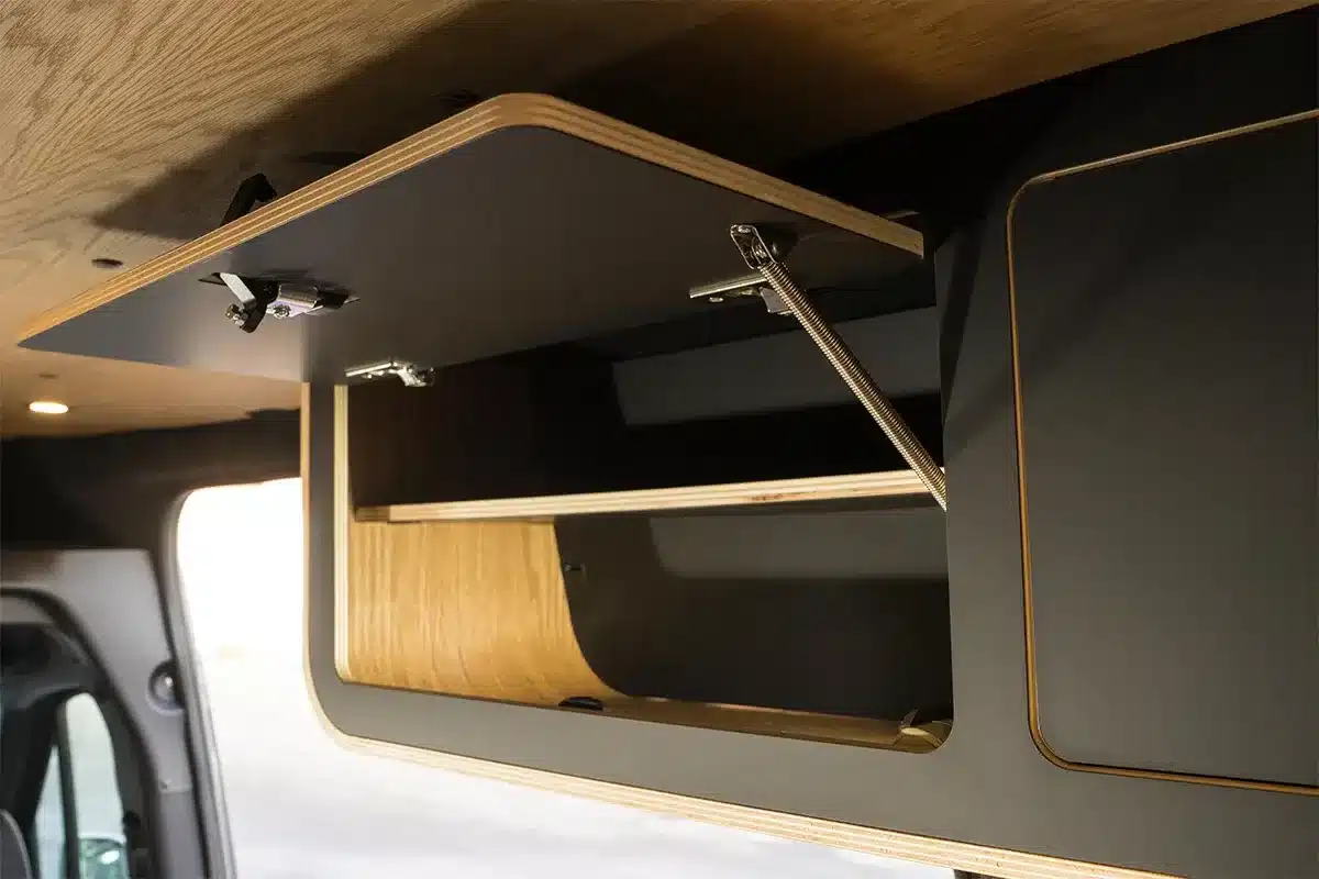 Geöffneter Campervan-Oberschrank mit dunkler Oberfläche und furniertem Holz im Van in Black.