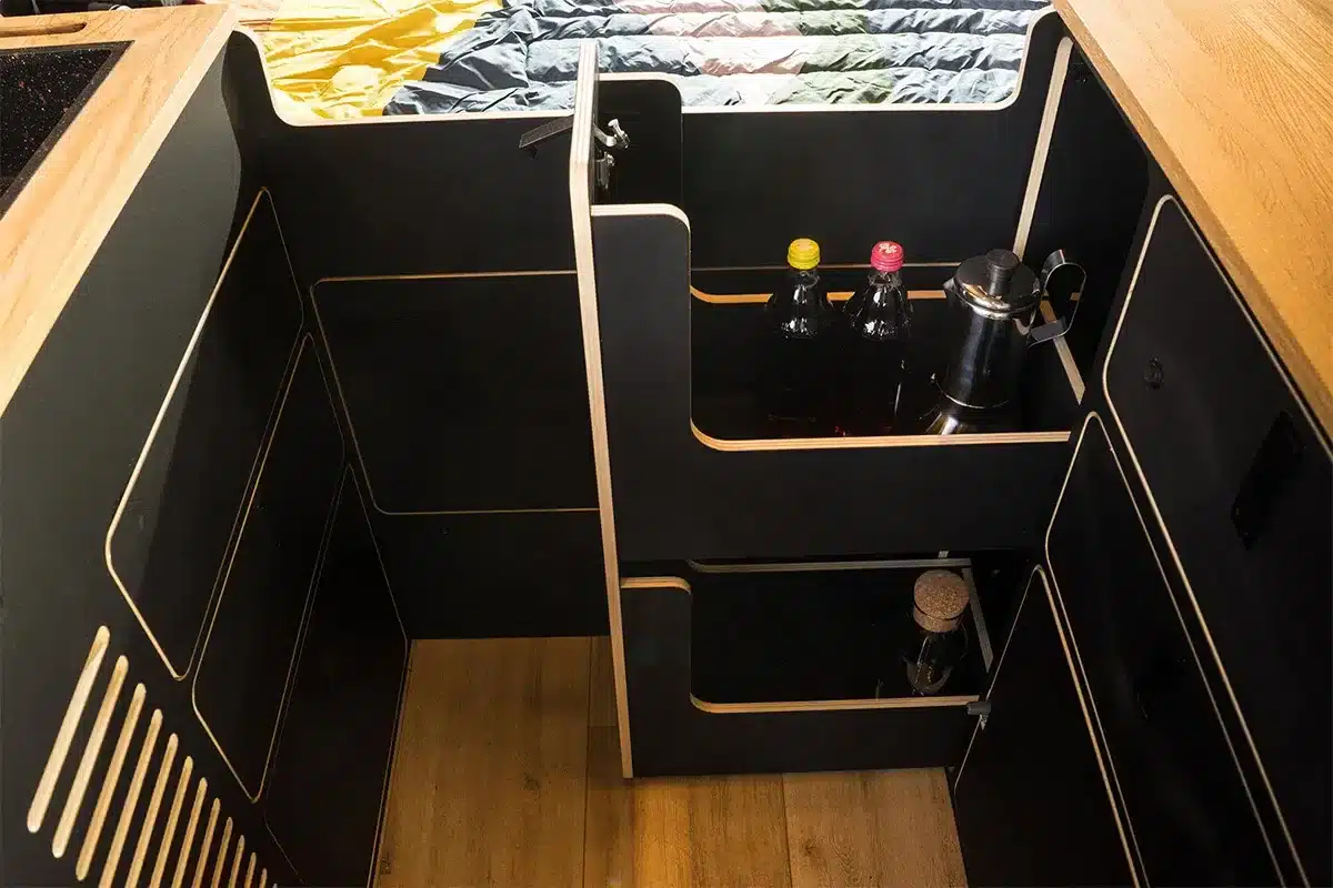 Stauraum mit schwarzen Oberflächen und Holzdetails sowie mehreren Flaschen im Van in Black Innenausbau