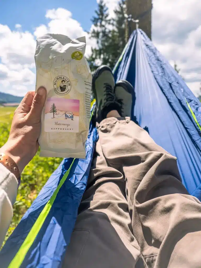 Person hält eine Packung 'Unterwegs' Outdoor-Kaffee von Murnauer Kaffeerösterei in einer Hängematte im Grünen