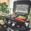 WAYNE 2-Brenner Gasgrill mit geöffnetem Deckel beim Grillen von Fleisch, Paprika und Spargel auf dem Balkon