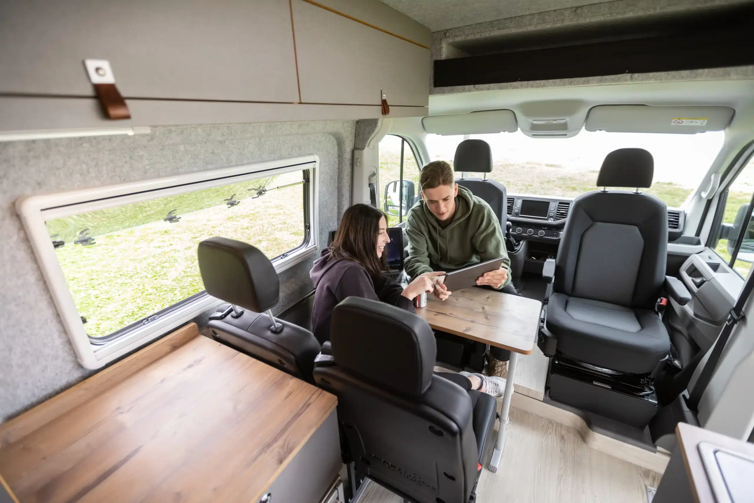 Innenansicht des WIGWAM Campervans mit zwei Personen an Tisch und drehbaren Vordersitzen.