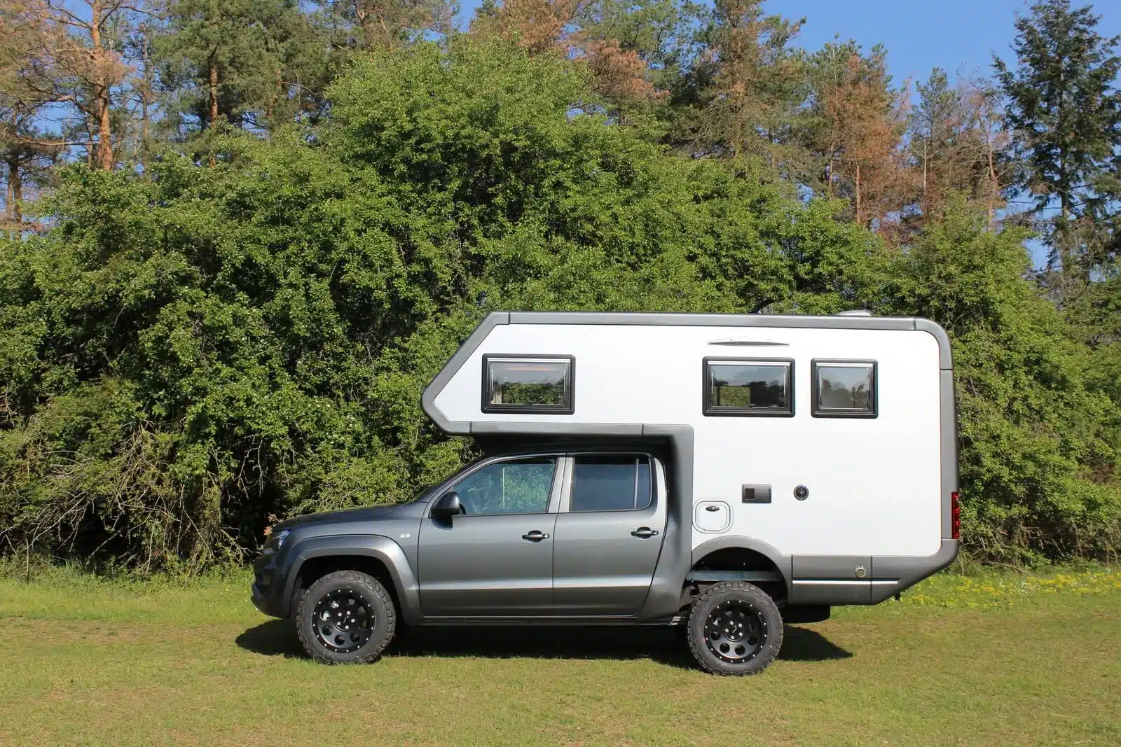 Seitenansicht eines Woelcke Autark Amarok 2019 Offroad-Campers auf VW Amarok, mit festem Wohnaufbau, stehend auf einer Wiese vor Bäumen.
