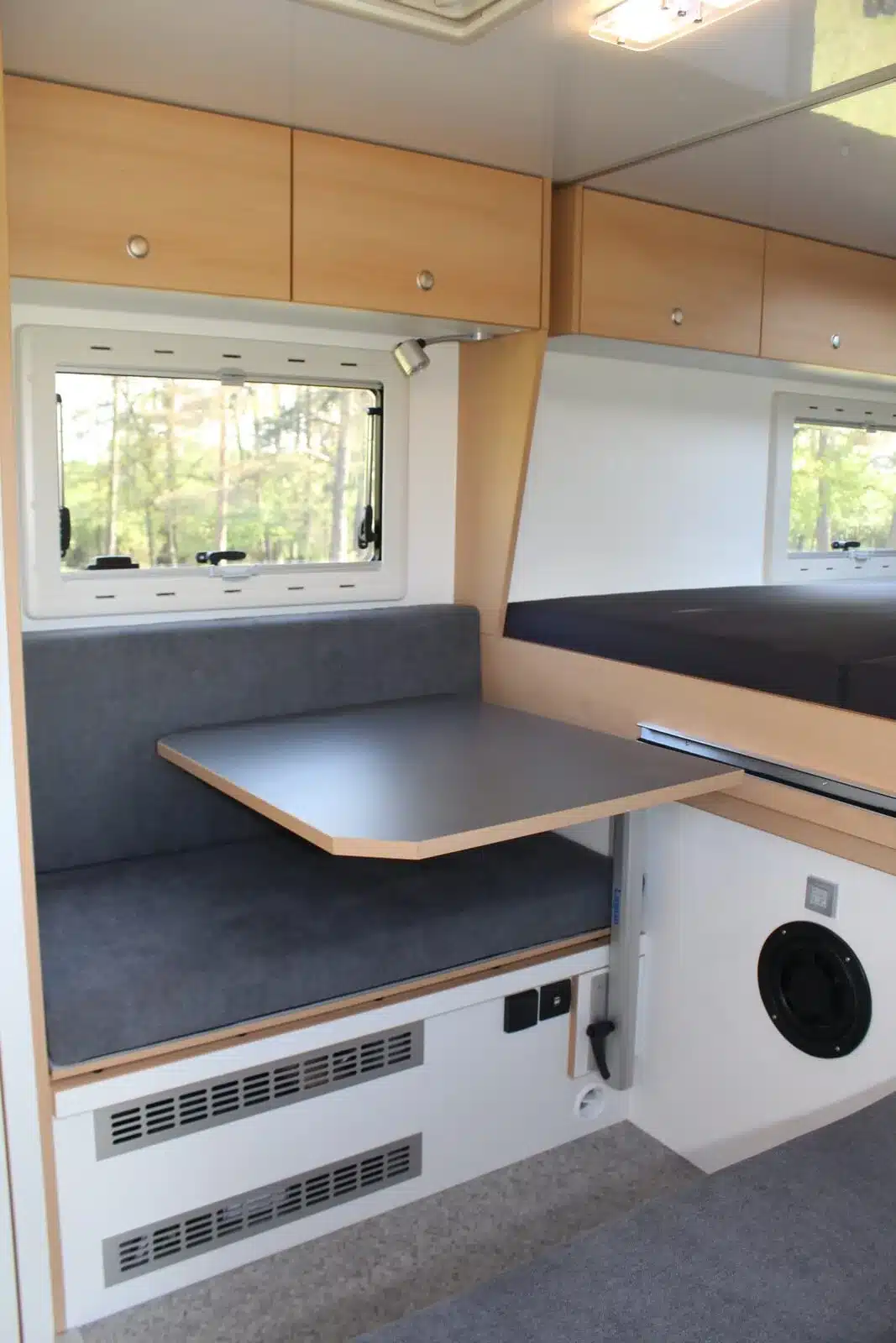 Kompakter Wohnbereich mit Sitzbank, Tisch und Alkovenbett im Woelcke Autark Amarok 2019