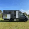 Seitenansicht eines Woelcke Autark Crafter C6 Allrad-Wohnmobils, aufgenommen draußen in der Natur bei blauem Himmel.