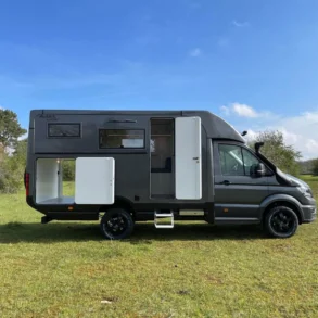 Seitenansicht eines Woelcke Autark Crafter C6 Allrad-Wohnmobils, aufgenommen draußen in der Natur bei blauem Himmel.