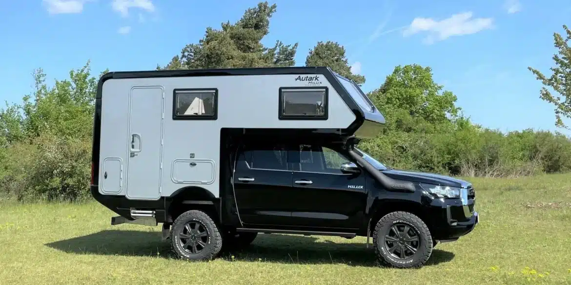 Schwarzer Toyota Hilux mit grauem Woelcke-Autark-Wohnaufbau auf einer Wiese