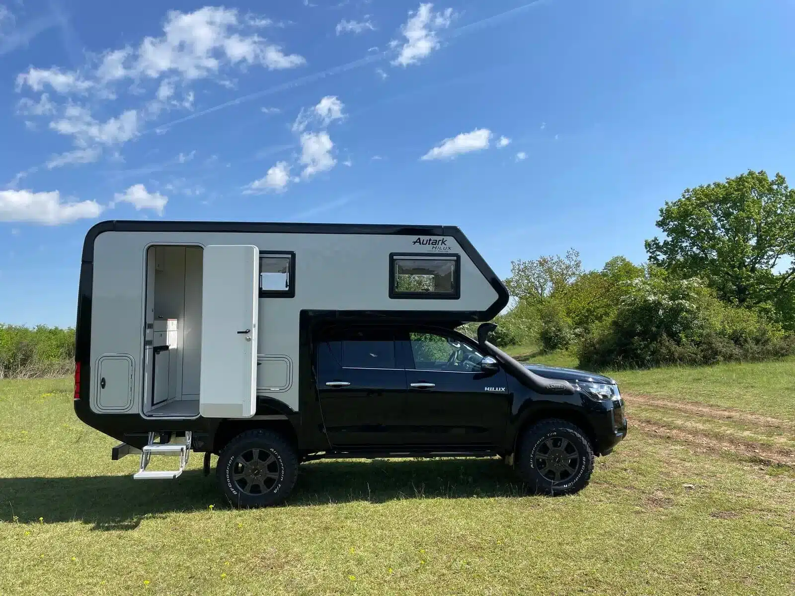 Schwarzer Woelcke Autark Hilux Double Cap 4x4 mit Wohnkabine auf einer Wiese